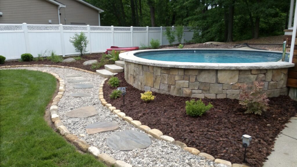 A backyard above-ground pool with a border made of gravel and mulch